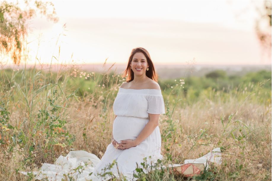 Posing for maternity photos a pregnant woman in a white dress sitting in a field