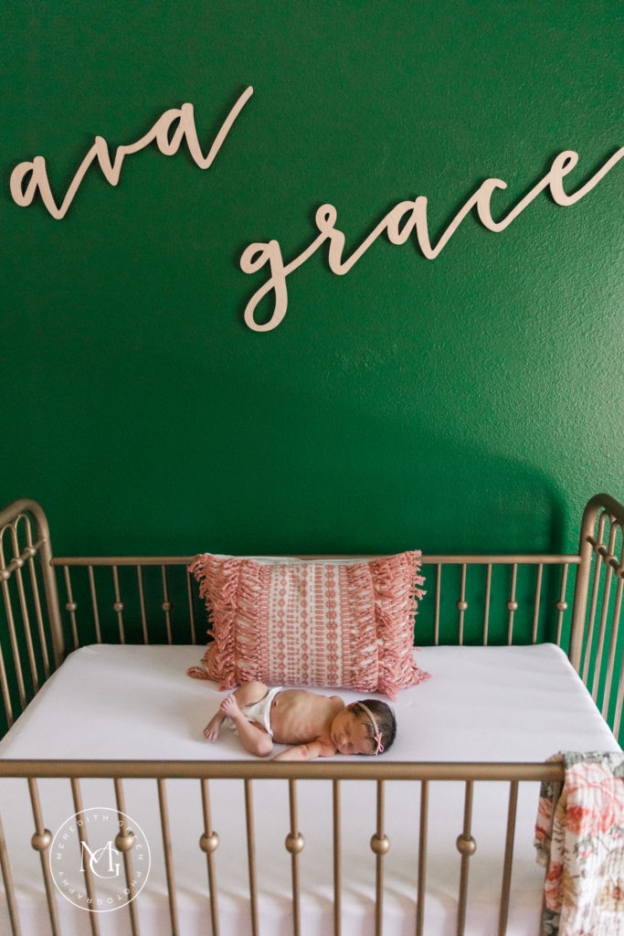 Crib with baby girl in front of green wall newborn lifestyle session