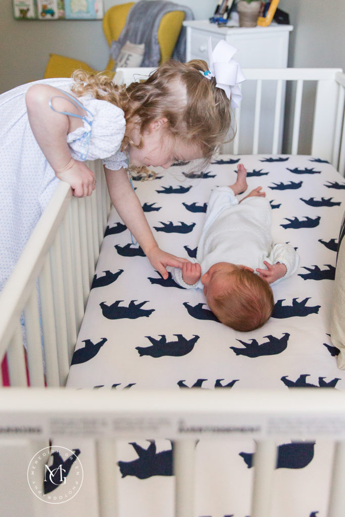 Sister touching baby in crib lifestyle newborn session