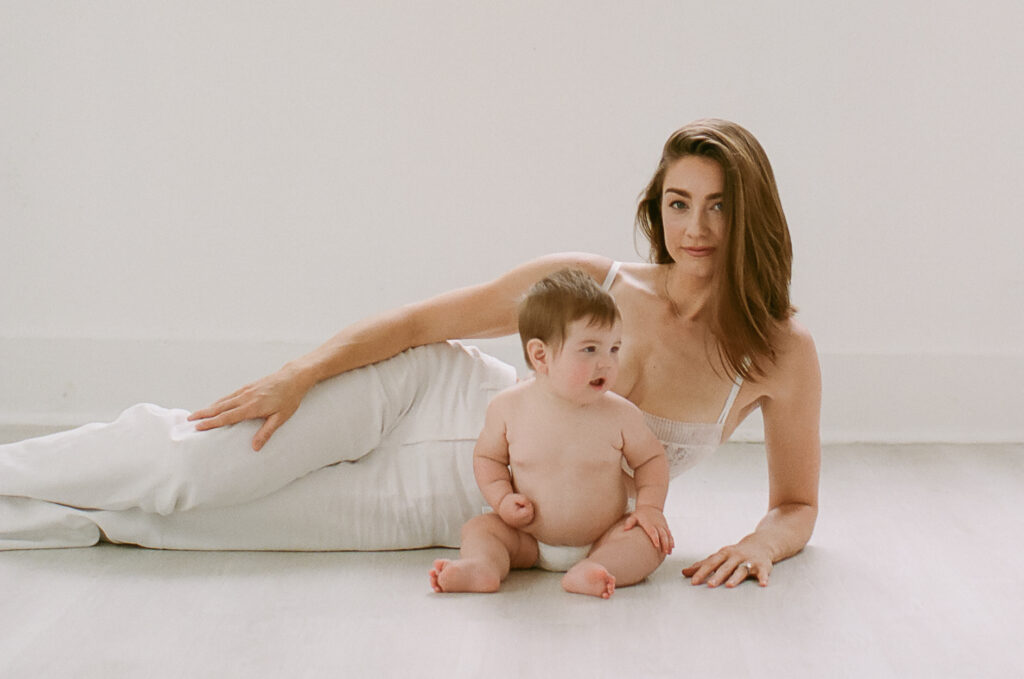 Mom laying on side with baby sitting in front of her looking at the camera