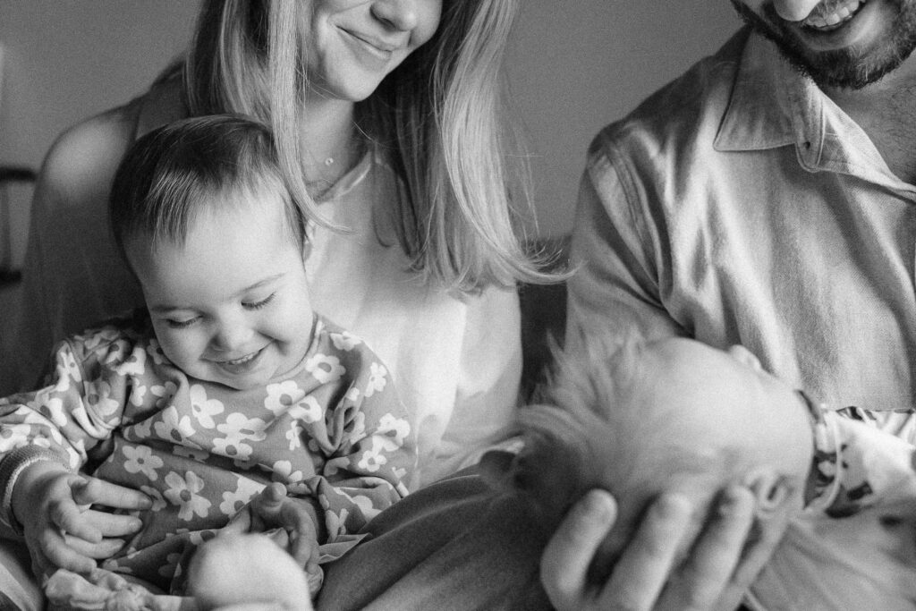 Family of four sitting together smiling at Sonny during newborn photos