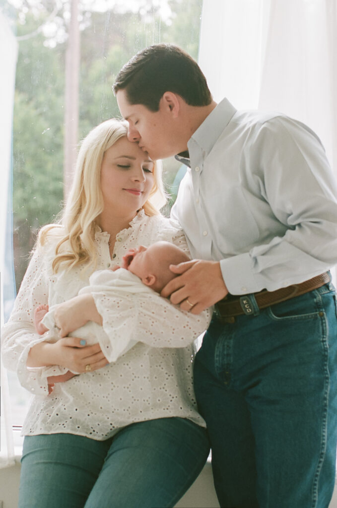 Mother and father standing near window holding newborn baby