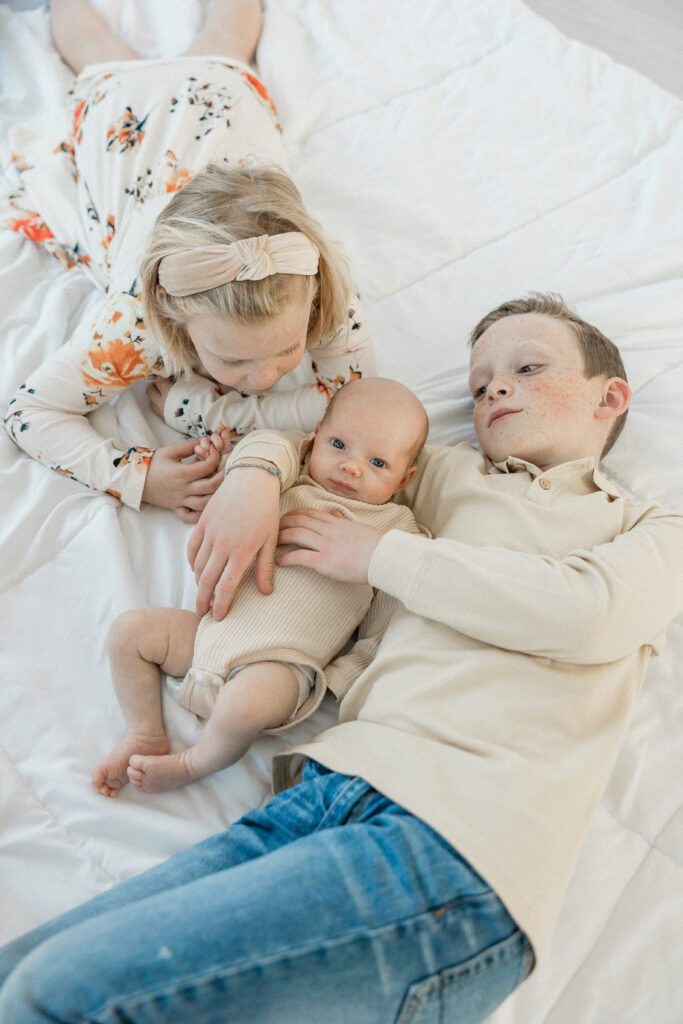 Older sister and brother cuddling with newborn sister